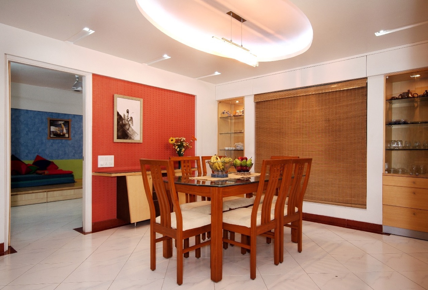 A teak dining set in front of a red accent wall and timber blinds